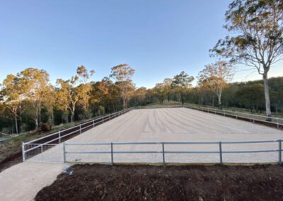 An empty outdoor sand horse riding arena surrounded by trees at dusk