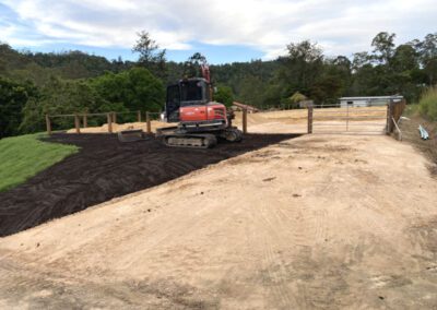 Excavator on a freshly leveled and landscaped rural area with trees in the background
