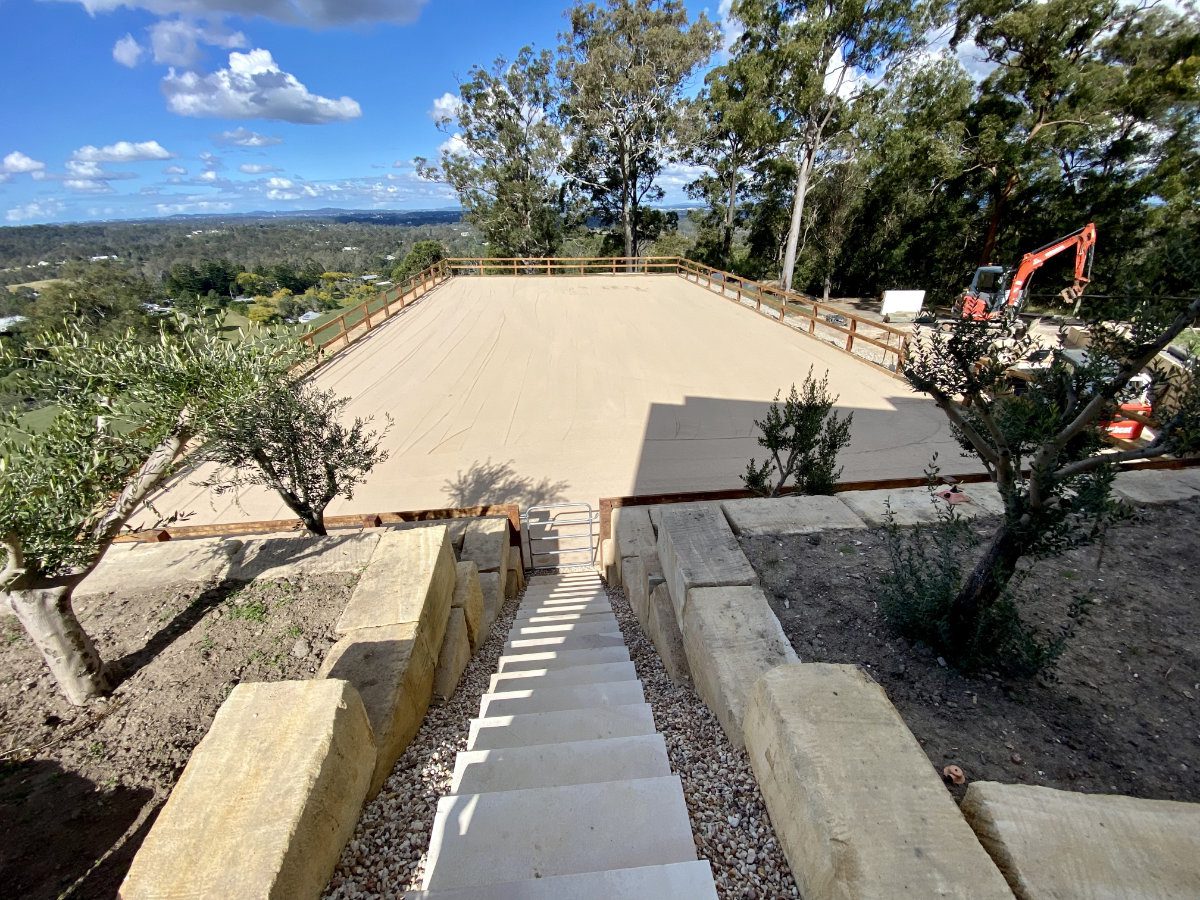 Large, newly constructed sandy court with surrounding trees and a staircase leading to it Large, newly constructed sandy court with surrounding trees and a staircase leading to it. Red excavator at a distance.