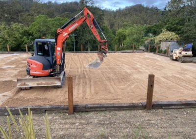 Red excavator on a freshly leveled construction site with trees in the background