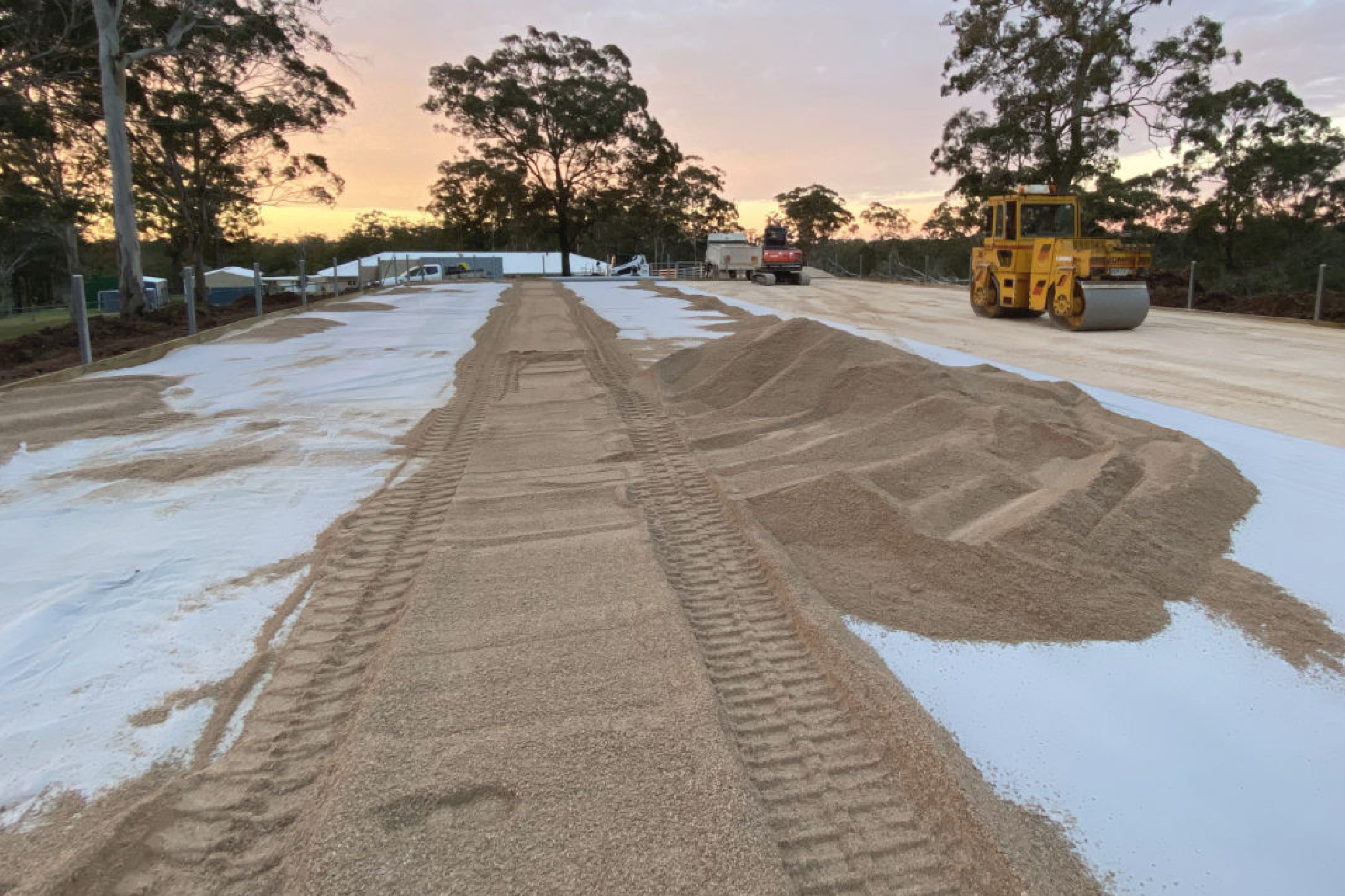 Road construction site with sand piles, heavy machinery, and tire tracks at dusk